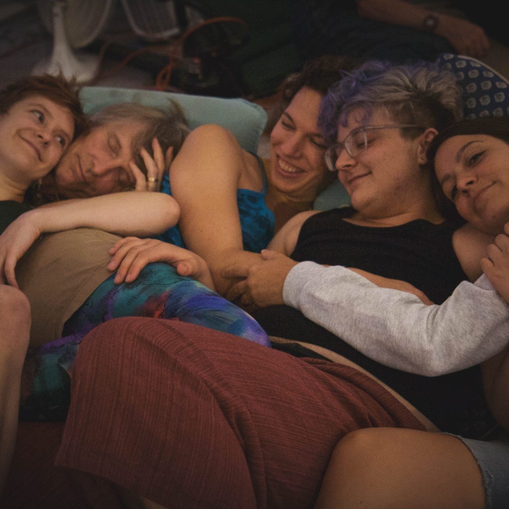 Five white people of diverse ages and genders in a cuddle pile.